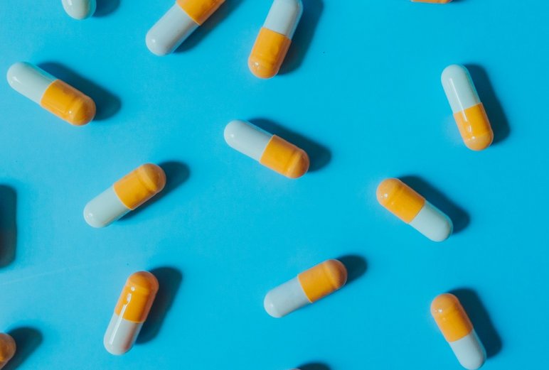 Various pills scattered across a blue background. Highlighting the multitude of applications related to automation and sample preparation in the clinical field, i.e., blood analyses, bacterial identifications or general lipidomics/metabolomics for precision medicine.