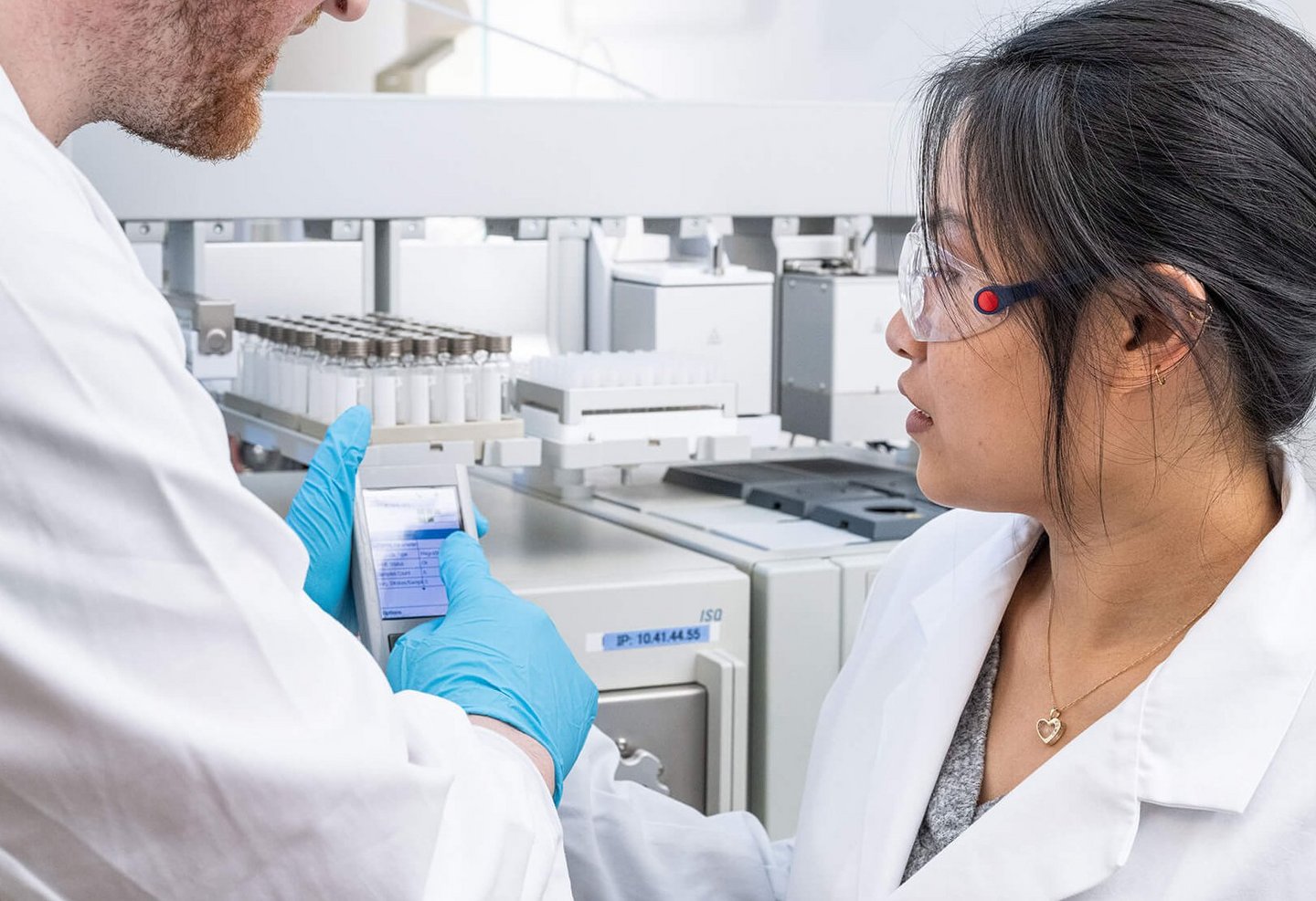 Happy user in a lab working with PAL System automation platform, reviewing data on a handheld device near sample trays.
